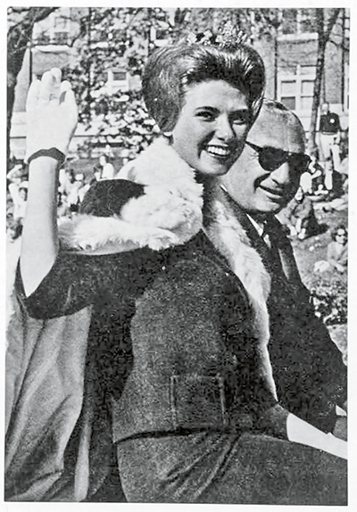 In a black-and-white photo, Andrea Hricko Hjelm waves during the Homecoming parade of 1962, where she served as Homecoming queen.