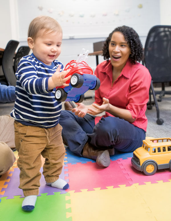 Photo of a toddler holding a toy next to postdoctoral researcher Charisse Pickron