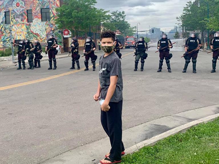 Young man wearing a mask and standing in front of a line of riot police