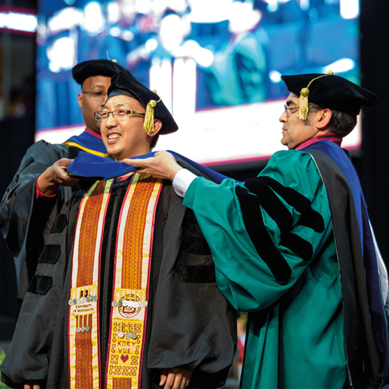 Michael helps graduating student Kory Vue with his regalia