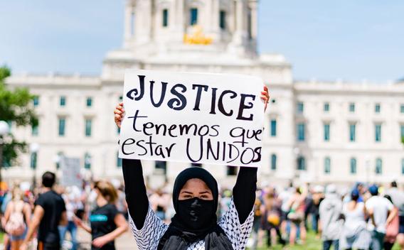 Woman holding sign with the word "justice" while standing in front of the Minnesota State Capitol