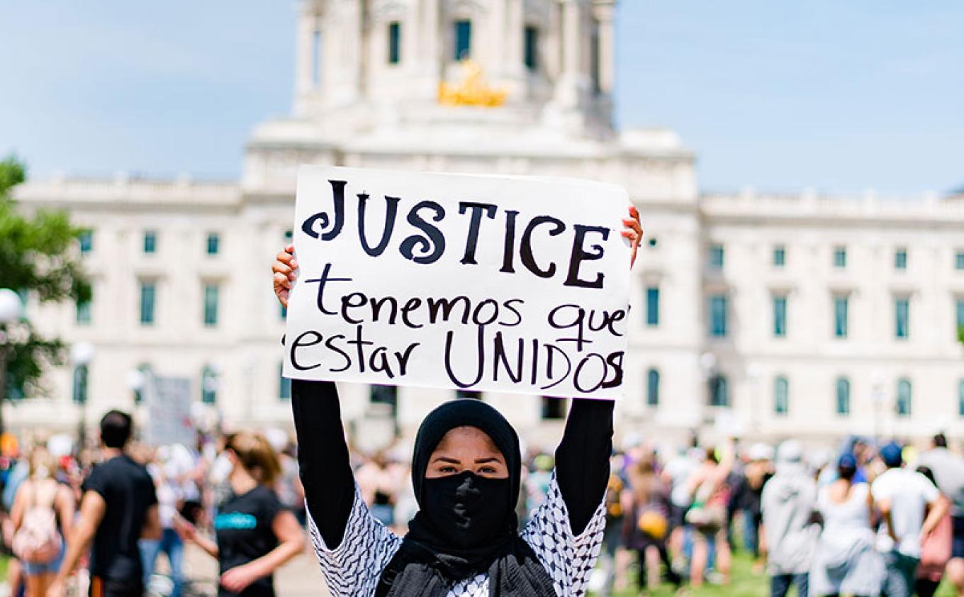 Woman holding sign with the word "justice" while standing in front of the Minnesota State Capitol