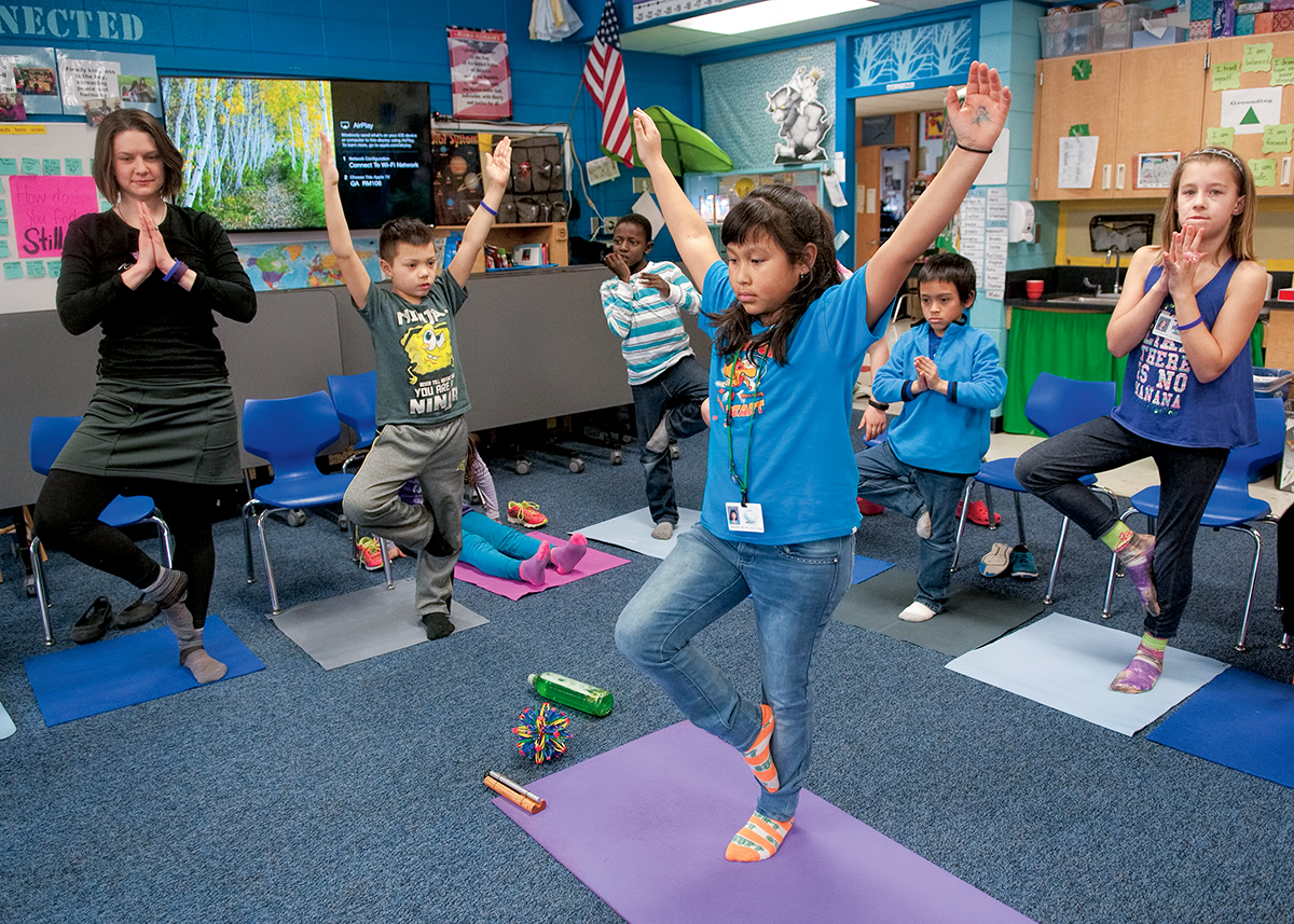 Photo: A student demonstrates the tree pose as teacher Stephanie Kennelly and classmates follow, using yoga mats inside of Kennelly's classroom.