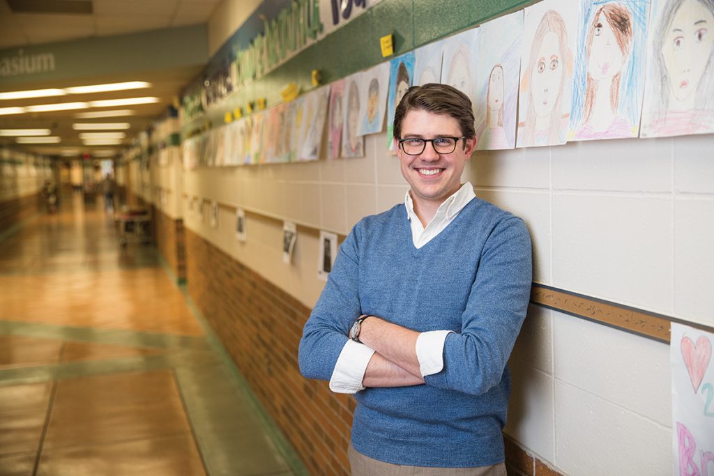 Greg Simonson poses in front of a wall lined with student artwork