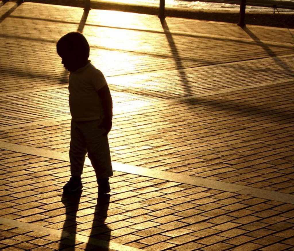 Color photo of a young child's silhouette, walking on brick pavement