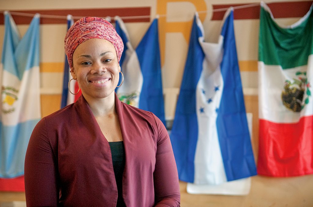 Jennifer Eik poses in her classroom, in front of a row of flags representing the countries of origin of her students