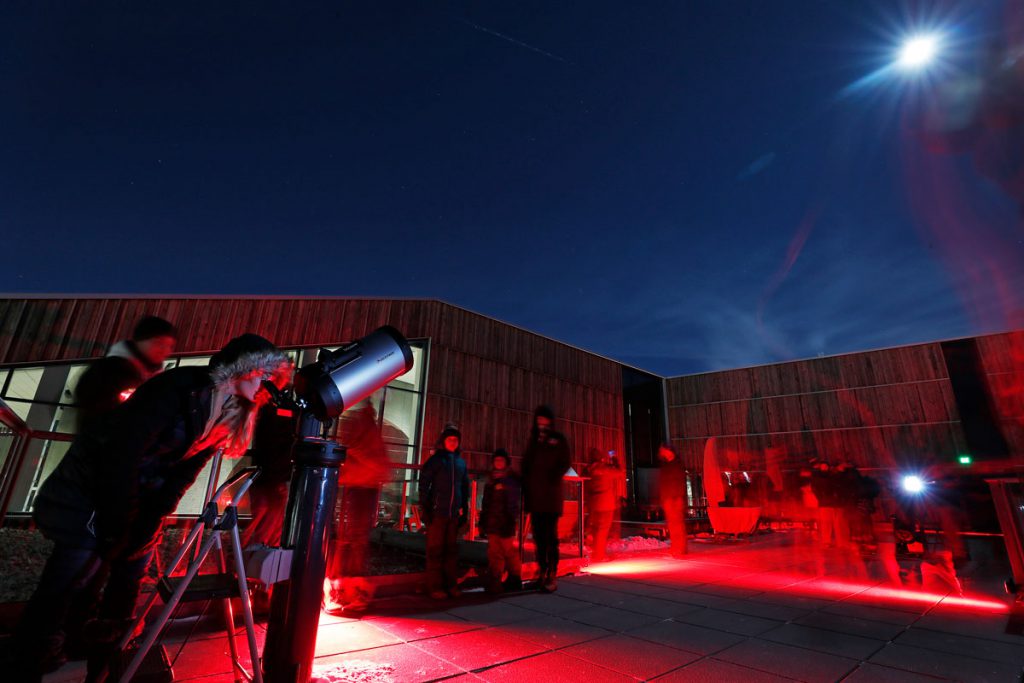 Night photo of people on the infrared-lit observatory deck of the Bell Museum under the eclipsed moon.