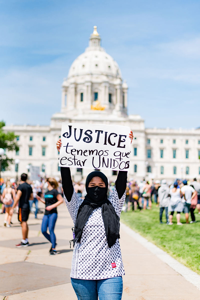 Woman holding sign with the word "justice" while standing in front of the Minnesota State Capitol