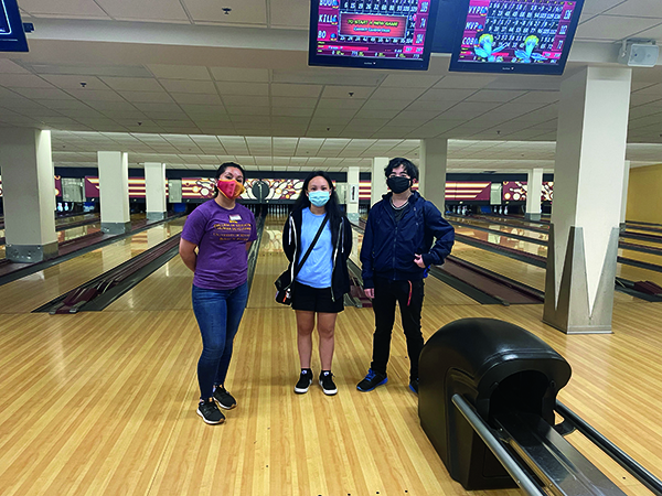 Three students posing in front of a bowling lane