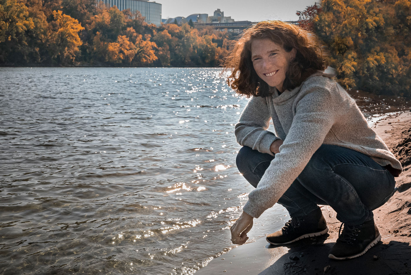 Student crouches near the banks of the Mississippi River on the University of Minnesota campus.
