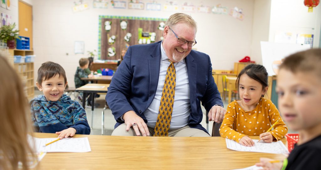 Superintendent is sitting at a table with four elementary school students